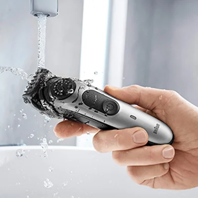 Braun trimmer being rinsed under running water, demonstrating its waterproof feature.
