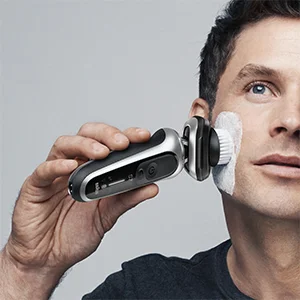 Man using a Braun electric shaver with a cleansing brush attachment on his face.