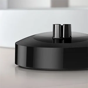 Braun toothbrush charger, black base with charging prongs, sitting on a reflective surface.