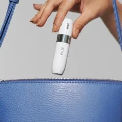 Braun mini hair remover being placed into a blue purse, highlighting its compact size.