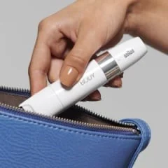 Braun Mini Hair Remover being placed into a blue purse, demonstrating its compact size.