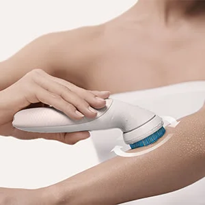 Braun cleansing brush being used on a woman's arm, with arrows indicating circular motion.