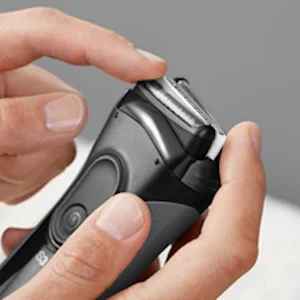 Braun electric shaver being held, with a finger pointing to the shaver head.