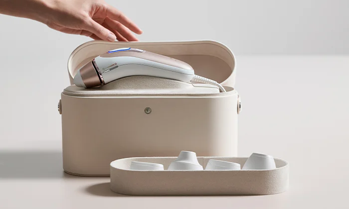 Hand opening a bag containing an IPL device, with a treatment attachments placed beside it.